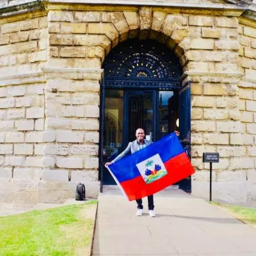Dr Pierre Michard Beaujour holding Haiti flag outside Bodleian Library